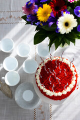 Bithday cake called Red Velvet with twisted silver candles on laid table with porcelain cups, saucers and colorful flower bouquet
