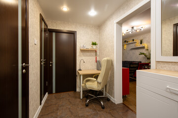 Apartment interior. Leather chair near a small desk. Desk lamp on the desk. Shelf on the wall. Compact work area in the hallway of a small apartment. Writing corner. Home mini-office.