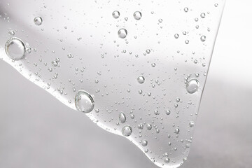 Liquid gel, hyaluronic acid flows down on gray background.