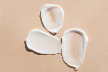 Samples of white cosmetic skin cream, foam on beige background, top view.