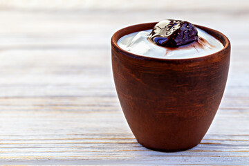 Clay cup filled with creamy sour cream or yogurt and topped with glossy strawberry jam on rustic wooden table. Delicious healthy breakfast with natural homemade feel, evoking countryside simplicity