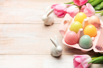 Easter eggs with ceramic bunnies and pink tulips decorating wooden table