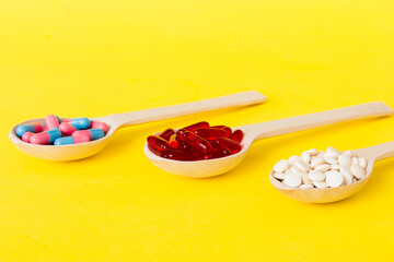 Vitamin capsules in a spoon on a colored background. Pills served as a healthy meal. Red soft gel vitamin supplement capsules on spoon