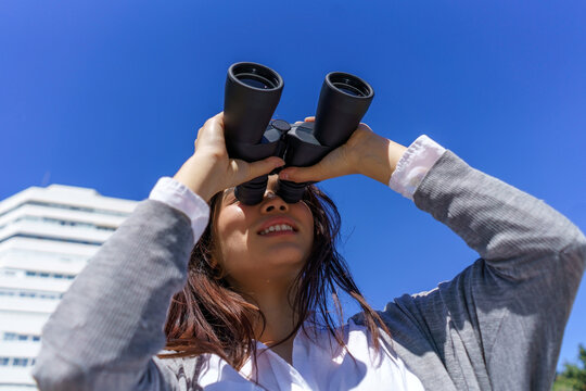 Japanese businesswoman holding binoculars looking for career opportunities under a blue sky