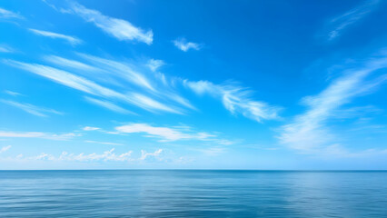Obraz premium Soft formations of delicate cirrus clouds drift gently across a vast, bright blue sky, overlooking a tranquil ocean expanse reaching towards a clear distant horizon