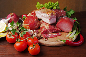 Meat products, bacon and sausages surrounded by vegetables and greens on a cutting board.