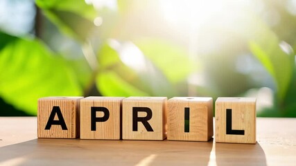 The month April in wooden blocks. Hello April text with fresh green leaves on the background. Sunlight shining in the spring