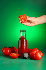 Woman squeezing tomato into bottle of ketchup on green background, closeup