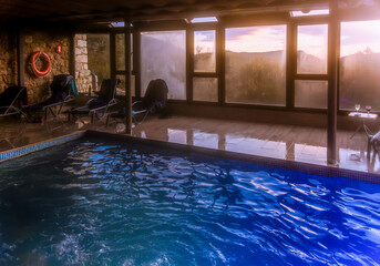 Indoor pool with views of the mountains at sunset through large windows.