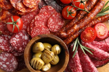 Different smoked sausages slices, olives, tomatoes and rosemary on table, closeup