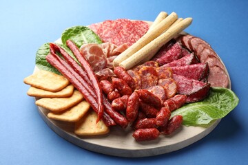 Different smoked sausages and other snacks on blue background, closeup