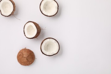 Halves of fresh coconuts on light background, flat lay. Space for text