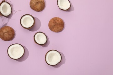 Pieces of cracked coconuts on violet background, flat lay. Space for text