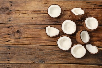 Pieces of cracked coconuts on wooden table, flat lay. Space for text