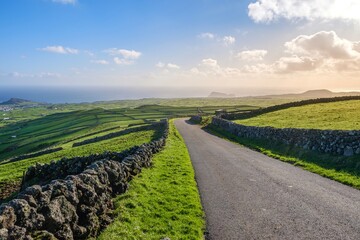 Serene rural scene in Terceira featuring a winding road through vibrant green patchwork fields,...