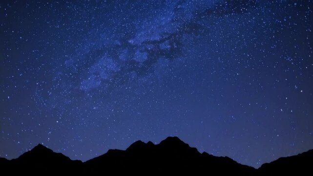 Timelapse of starry night sky over silhouetted mountains with milky way unveiling