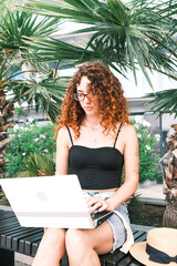 Blogger on vacation. A woman works on her laptop under the palm trees .