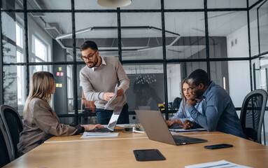 By the table. Professional workers are in the modern office together