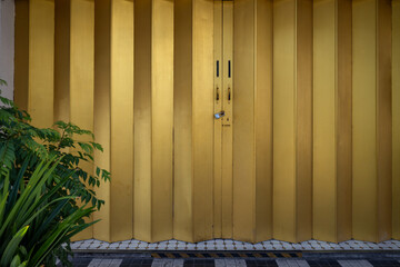 A straight-on view of a golden metal accordion-style gate with a plant in the foreground on the left