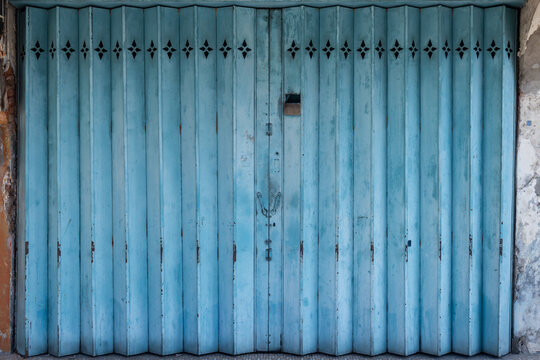A straight-on view of a dilapidated azure blue metal accordion-style gate