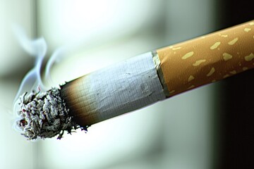 A close-up shot of a burning cigarette with smoke billowing, depicting addiction and the negative health effects, with a blurry background to highlight the burning cigarette.