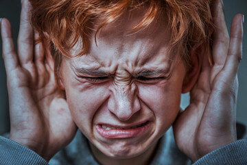 Close-up of a child with red hair covering ears with hands, showing distress, symbolizing anxiety, stress, or sensory overload