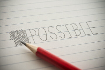 Close up pencil handwriting impossible change to possible via strikethrough on notepad background. Changing impossible to possible philosophy, motivation, problem solution, business target concept.