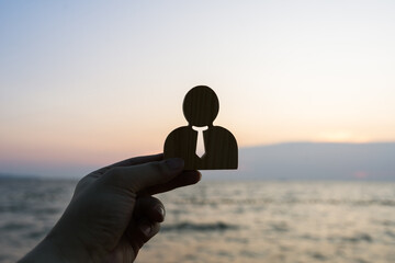 Businessman symbol raised against a sunset sea background. Concept of work stress, corporate...