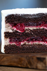 A piece of delicious cherry cake. Close-up, layers of cream, compote and chocolate sponge cake.