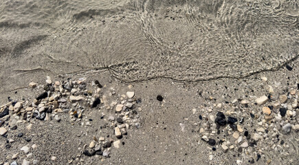 sandy beach with crystal clear water ripples and small pebbles. under clear ripples. natural background with copy space. stone background