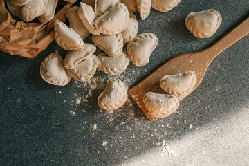 Top view of raw homemade dumplings scattered on a floured surface with wooden spatula and paper bag — traditional Eastern European cooking scene