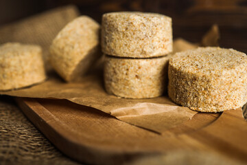 Raw breaded cutlets prepared for frying, stacked on parchment paper and wooden board. Frozen semi-finished meat product on a dark rustic kitchen background
