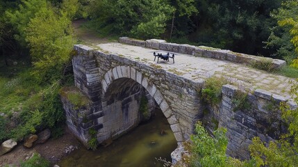 Fototapeta premium Drone surveys historic stone bridge amidst vibrant, verdant woodland scenery