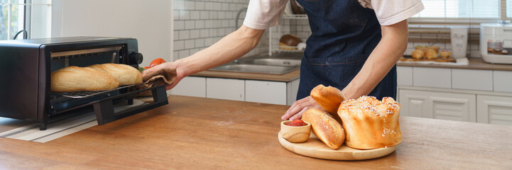 Young man baking bread using small oven in cozy home kitchen with natural window light and modern interior