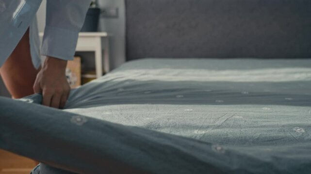 An individual making a bed. The person adjusts the sheets and comforter, creating a neat and inviting atmosphere in the cozy bedroom.