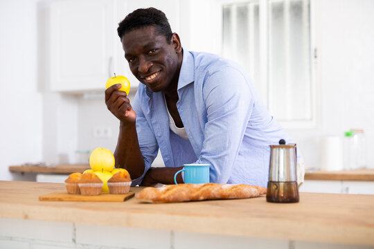 Smiling african american man eating apple in home kitchen