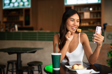 Young woman in cafe eating dessert and taking selfie