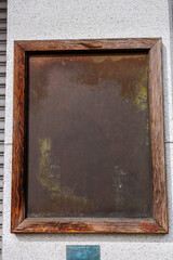 A rustic wooden frame encases a weathered, dark surface mounted on a stone wall. The frame's grain and knots add character to the minimalist and aged appearance.