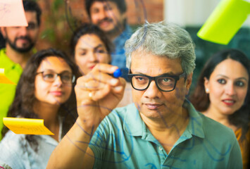Young Indian entrepreneurs discussing strategies using marker pens and stickers on a glass wall