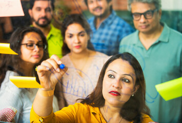 Young Indian entrepreneurs discussing strategies using marker pens and stickers on a glass wall