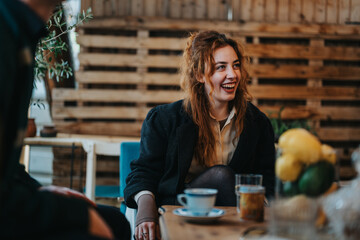 A young woman laughs warmly while sitting in a inviting cafe environment, surrounded by decor and cozy ambiance. The moment captures a joyful and friendly atmosphere of connection and comfort.