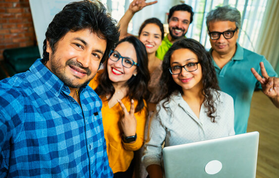 Young Indian Asian businessman capturing a selfie with his startup team in a creative workspace
