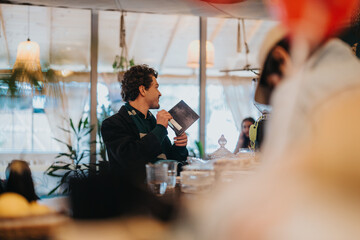 A casually dressed man examines a menu in a warmly-lit coffee shop with a vibrant and relaxed atmosphere. Surrounding details include greenery, wooden decor, and a welcoming ambiance.