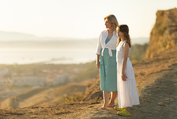Mother and daughter admiring inspiring sunset landscape from hilltop