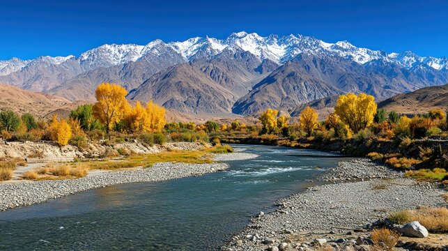 Autumnal river valley nestled between mountains with snow-capped peaks. Golden foliage lines the riverbank