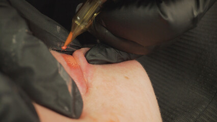 Professional beautician carefully applying permanent makeup tattoo on woman's lips using...