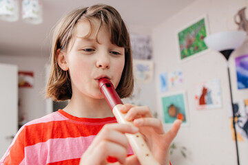 A teenage girl plays a musical instrument, the flute, in her room at home. Music lessons at home. Hobbies of teenagers © Elena Medoks