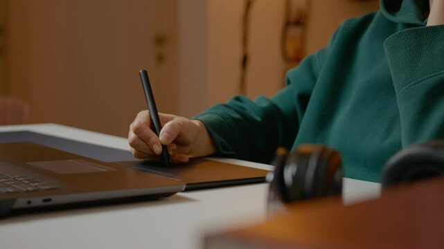 Graphic designer creating digital artwork using pen tablet and laptop while working intently from home office with professional focus