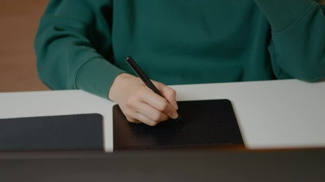 Graphic designer focuses on creating illustrations using a pen display and laptop in a cozy home office setting. The process showcases digital artistry and technology.