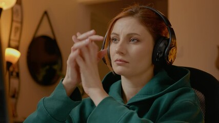 Woman wearing headphones intently watches her laptop screen in a cozy home office. She appears deep in thought, fully engaged with her work or content.
